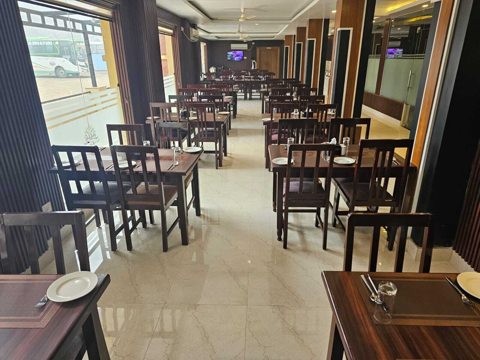 A restaurant with a long counter and multiple tables, a television mounted on the wall, and a view of the street outside.