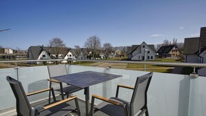 A balcony with a table and chairs, overlooking a residential area with houses and a clear sky. - Beachfront vacation rental with a balcony, access to the pool and sauna - Rex Rugia (Mönchgut OT Lobbe)