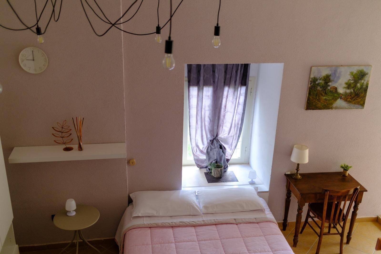A bedroom with a bed, bedside table, lamp, and a window with curtains.