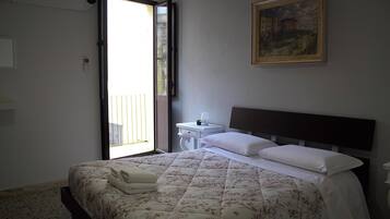 Una habitación de hotel con una cama, una mesita de noche, un cuadro en la pared y una puerta que da a un espacio al aire libre.