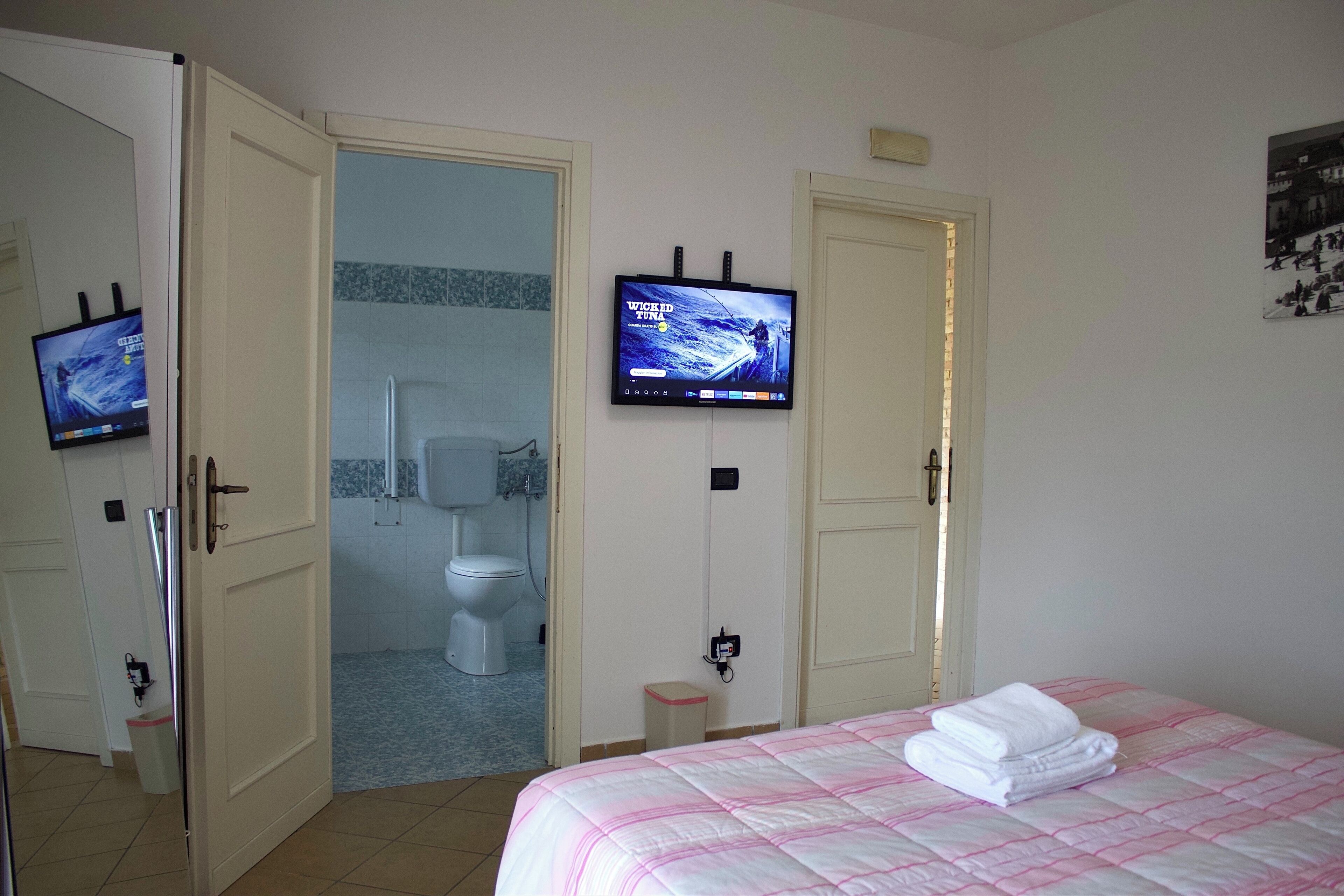 Habitación de hotel con una cama, un televisor fijado a la pared y un baño visible a través de una puerta abierta.