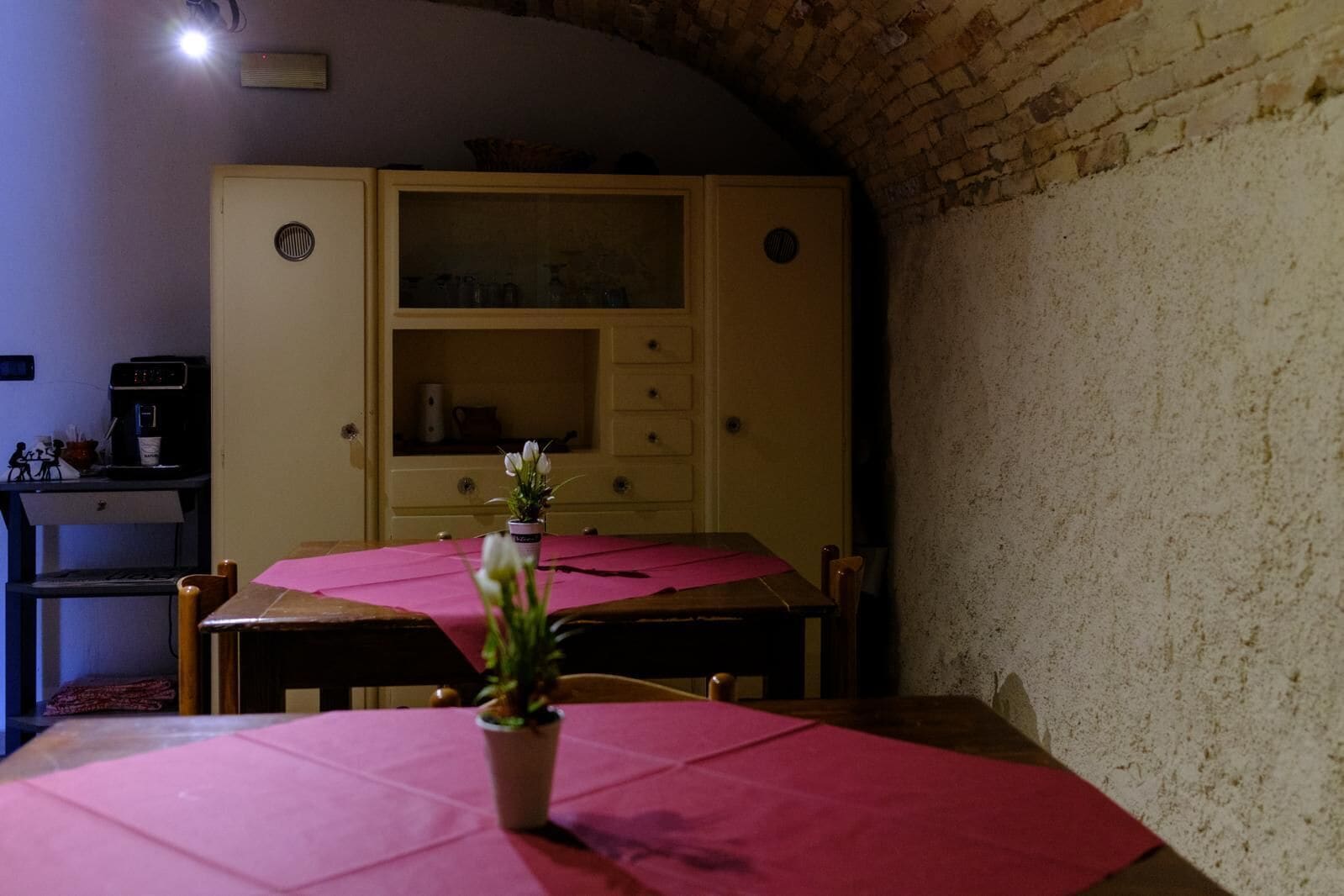Una stanza con un tavolo da pranzo ricoperto da una tovaglia rosa, una pianta in vaso sul tavolo e un mobiletto in legno con vetrate sullo sfondo.