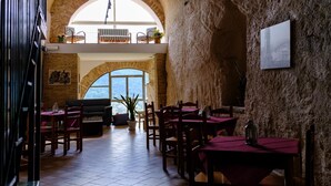 A restaurant with high arched stone walls, wooden tables, and chairs. There is a large window providing natural light and a view of the outdoors. - Il castello di atessa  (Atessa)