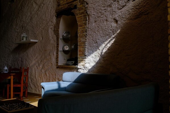 Una habitación acogedora con pared de ladrillo, una silla de madera, un sofá azul y una pequeña mesa con un tablero de ajedrez.