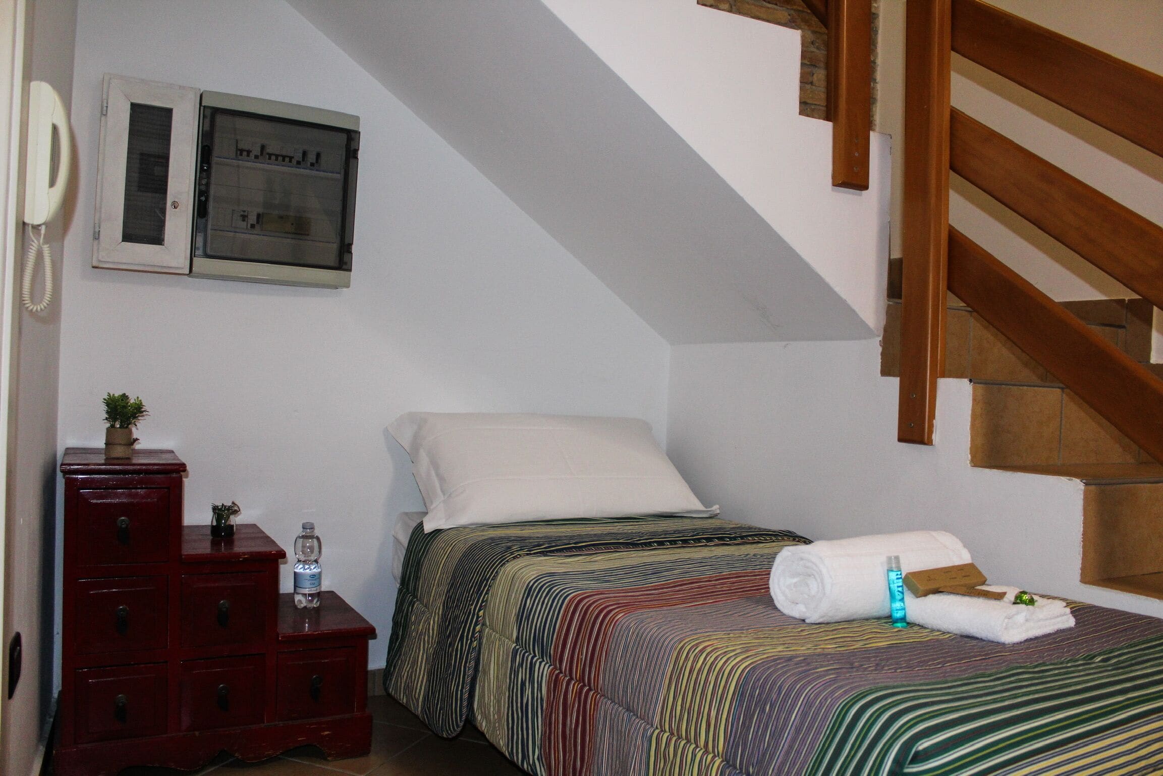 A bedroom with a bed, a dresser, a telephone, and a staircase.