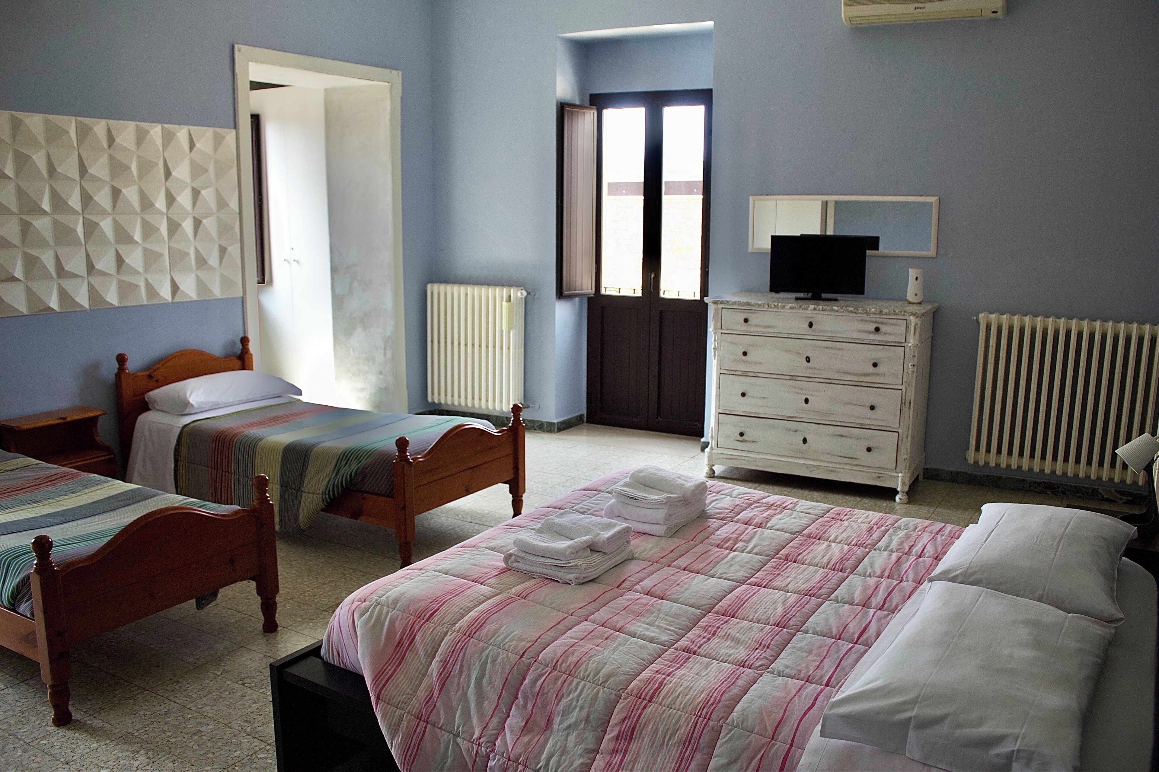 A bedroom with two beds, a dresser, a radiator, and a television.