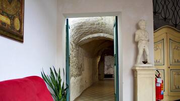 A hallway with a stone archway leading to another room, a red sofa, a potted plant, and a statue on a pedestal.
