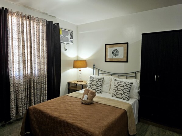 A bedroom with a bed, a bedside table with a lamp, a framed picture on the wall, and a wardrobe.
