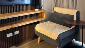 Una sala de estar moderna con un televisor de pantalla plana montado en una pared de paneles de madera, un sofá cómodo, una mesita y una ventana con cortinas.