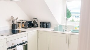 Una cocina con armarios blancos, horno empotrado, hervidor y una ventana con vistas a un edificio.