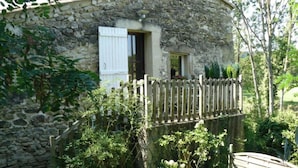 Una casa in pietra con recinzione in legno, un piccolo portico e vegetazione rigogliosa.