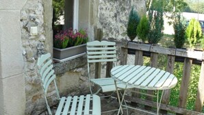 Una veranda con due sedie in metallo bianco e un tavolo, affacciata su un muro in pietra con un recinto in legno e vegetazione sullo sfondo.