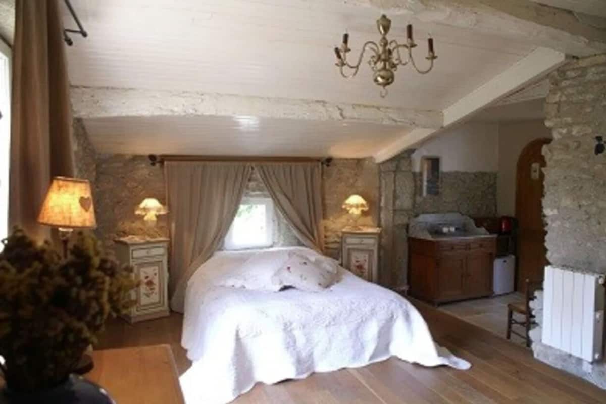 A bedroom with a bed, a nightstand, a lamp, a dresser, and a chandelier.