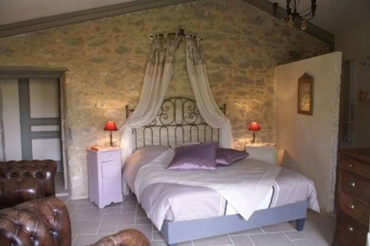 A bedroom with a stone wall, a four-poster bed, two bedside tables with lamps, and a wooden dresser.