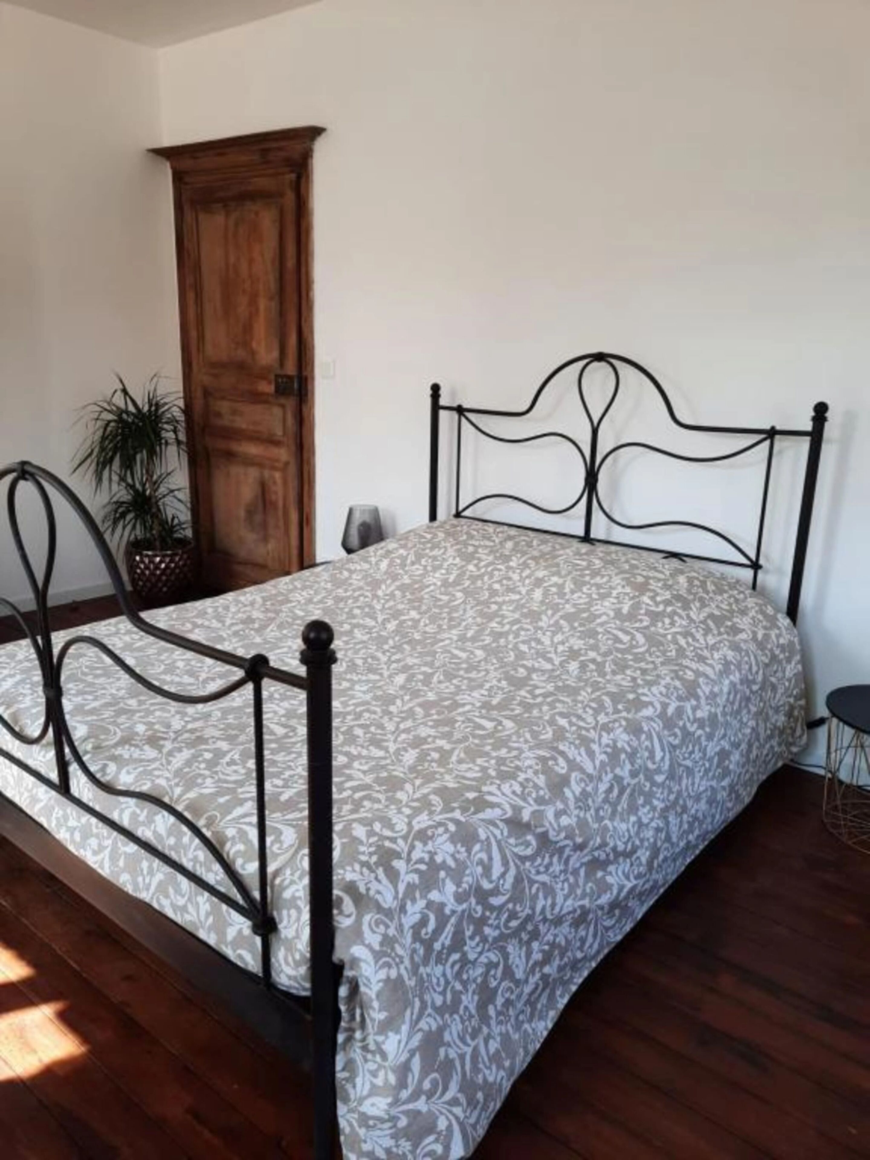 Una cama individual con estructura metálica y colcha estampada en una habitación con suelo de madera y un armario de madera.
