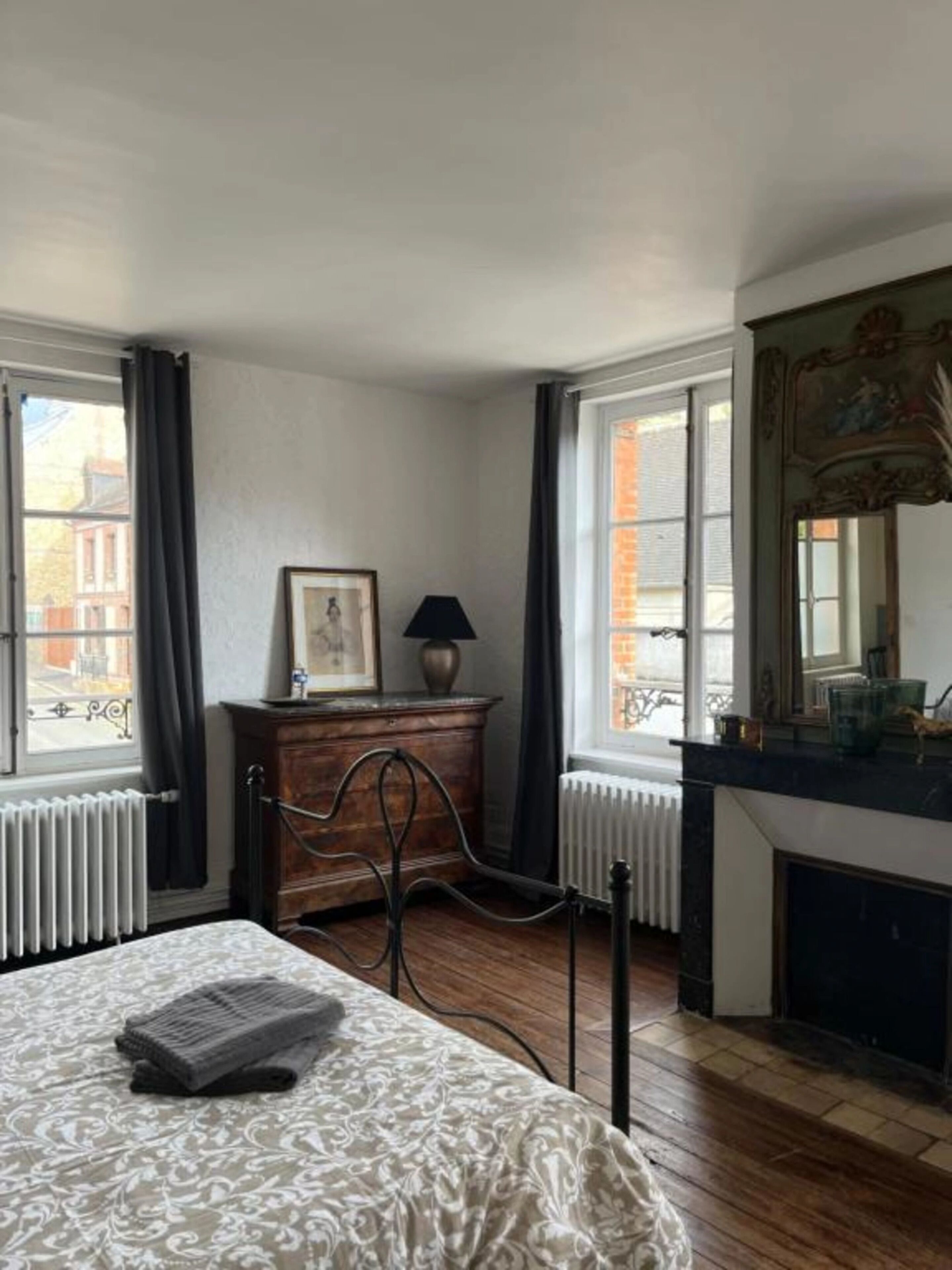 Une chambre d’hôtel avec un lit, une commode, une cheminée et une fenêtre donnant sur des immeubles.