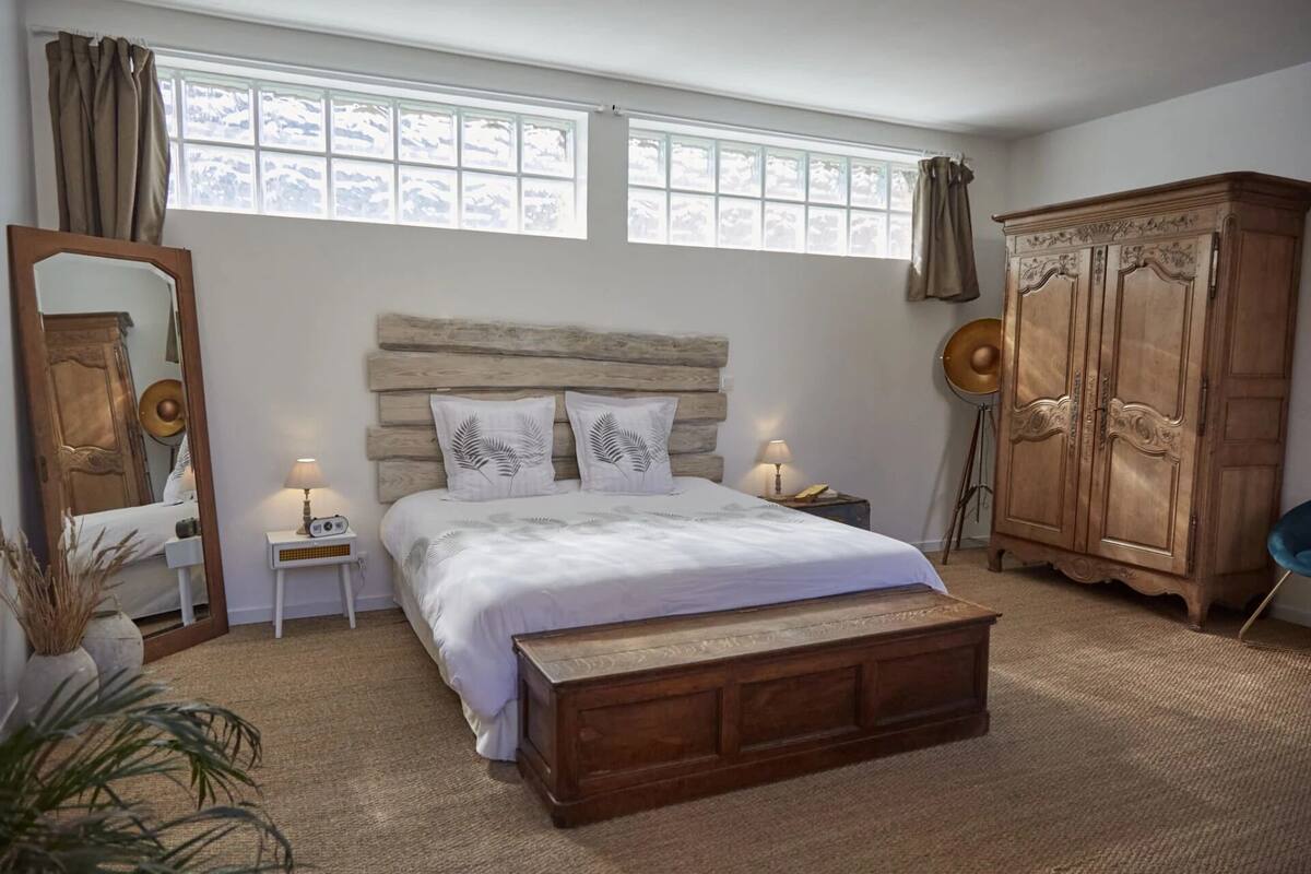 A bedroom with a large bed, a wooden headboard, a wardrobe, and a mirror.
