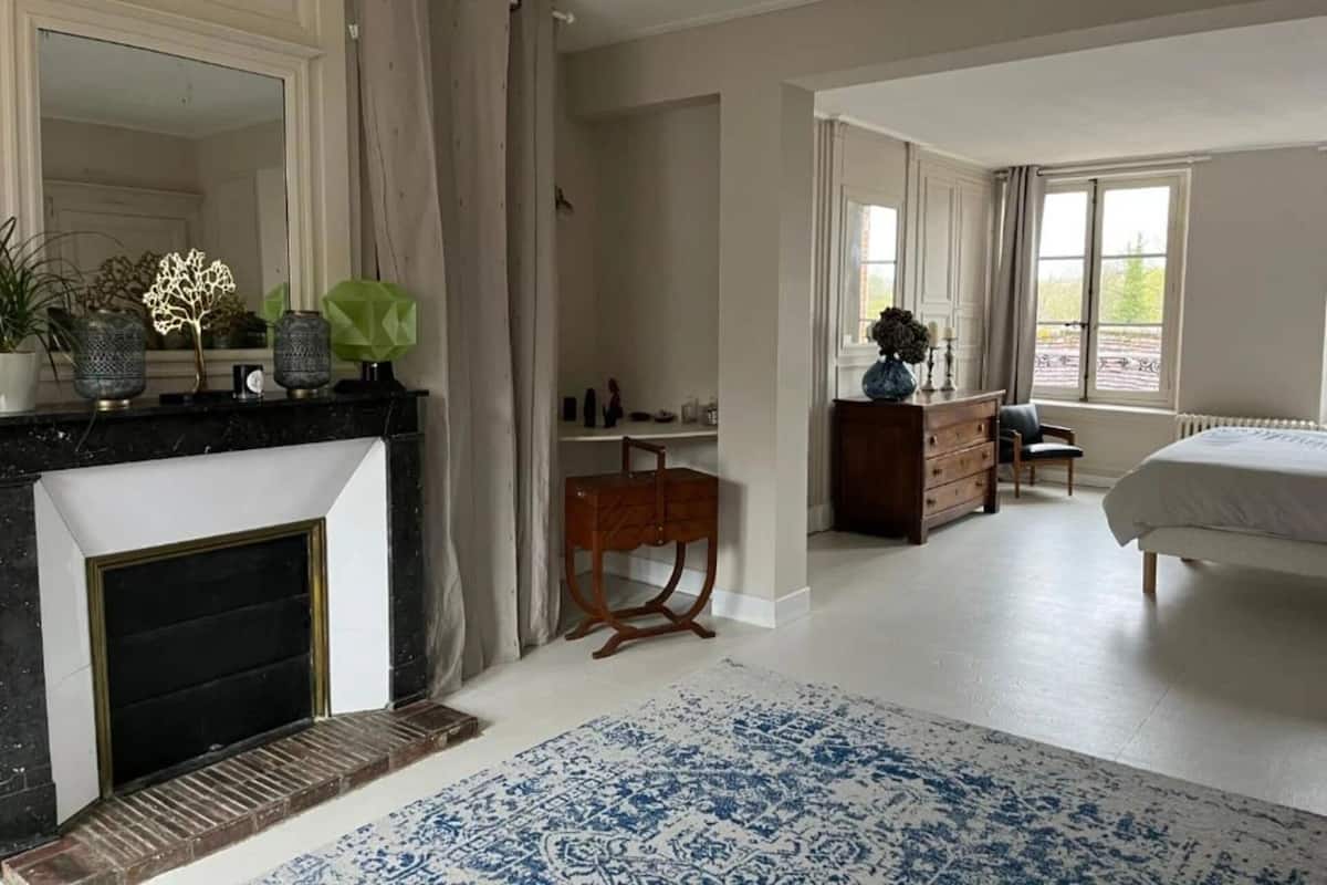 A bedroom with a large bed, a dresser, a vanity, and a fireplace.