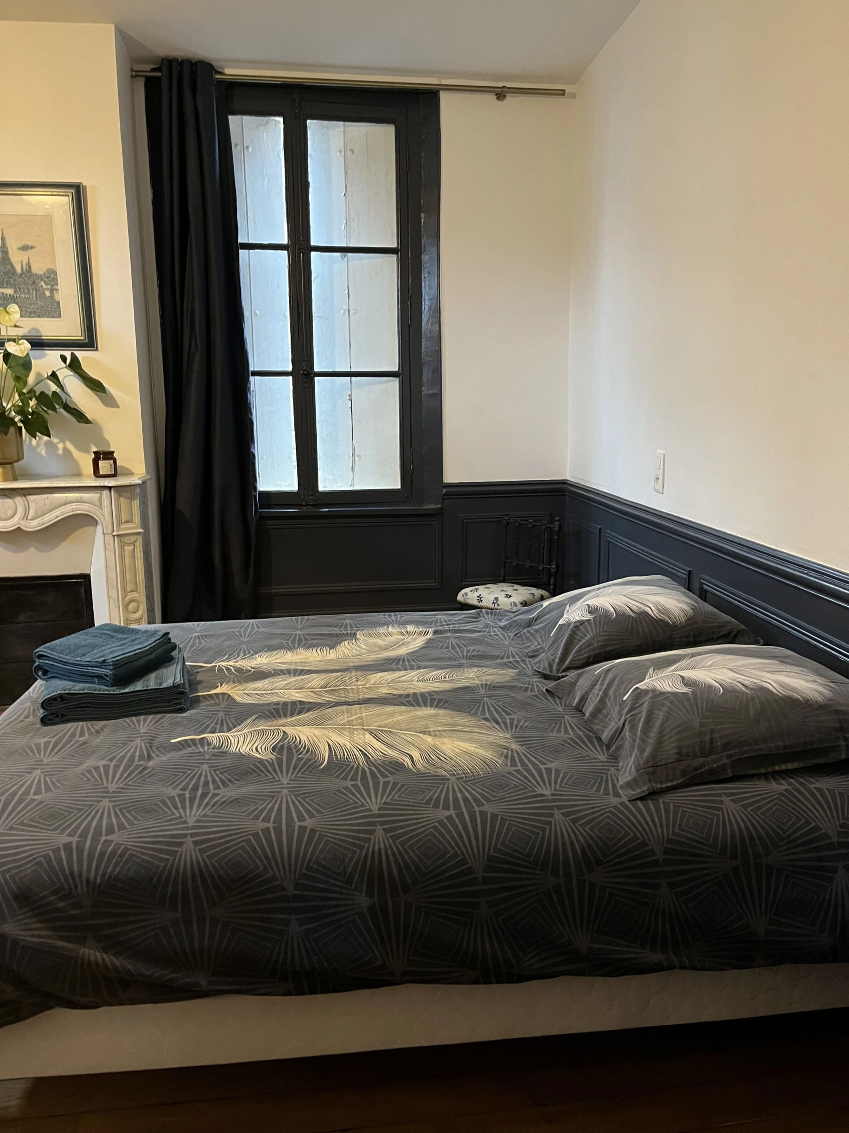A bedroom with a bed, a window with curtains, a nightstand, and a framed picture on the wall.