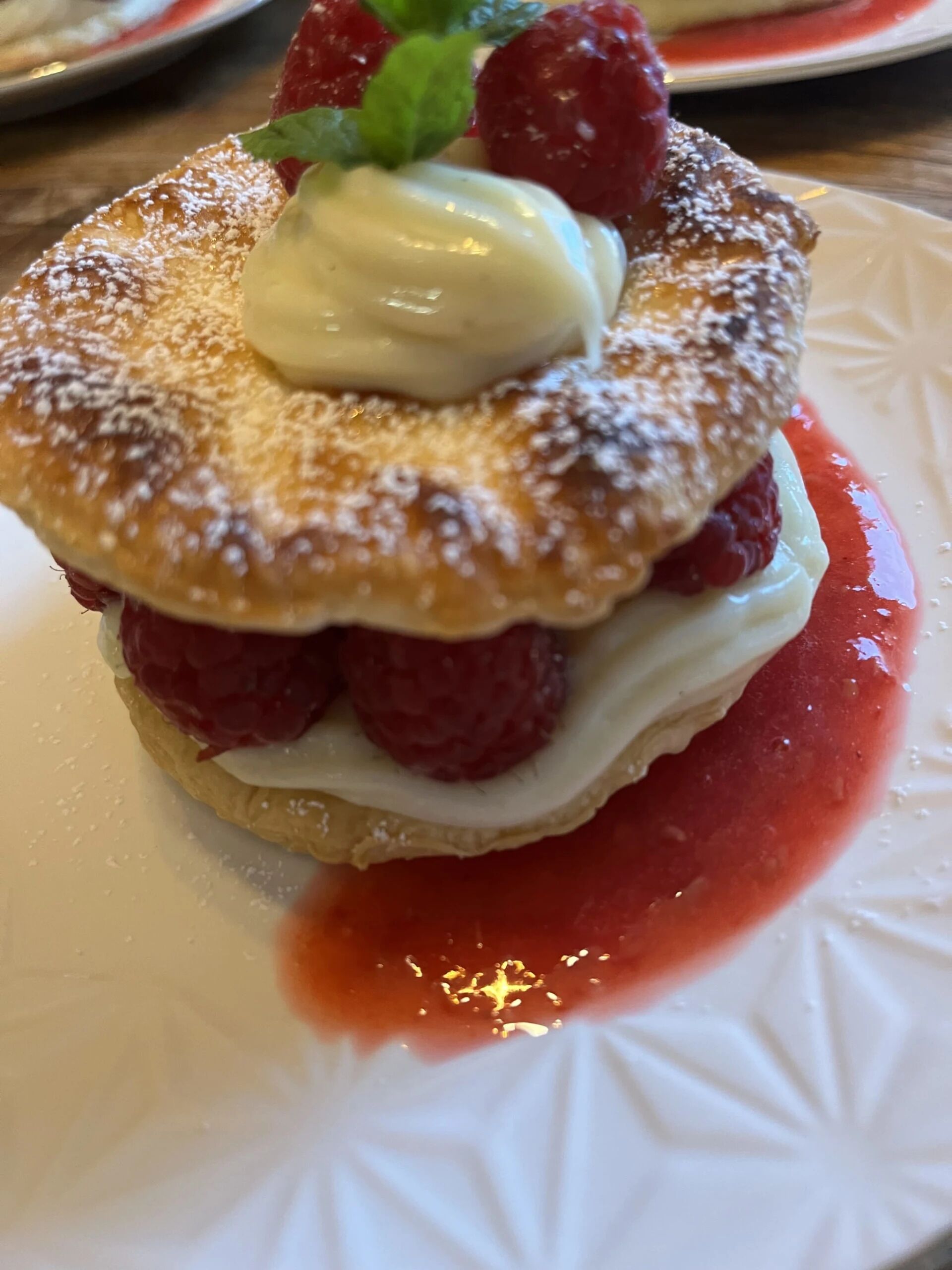 En dessert med vispad grädde, hallon och ett lätt puder av florsocker, serverad på en tallrik.