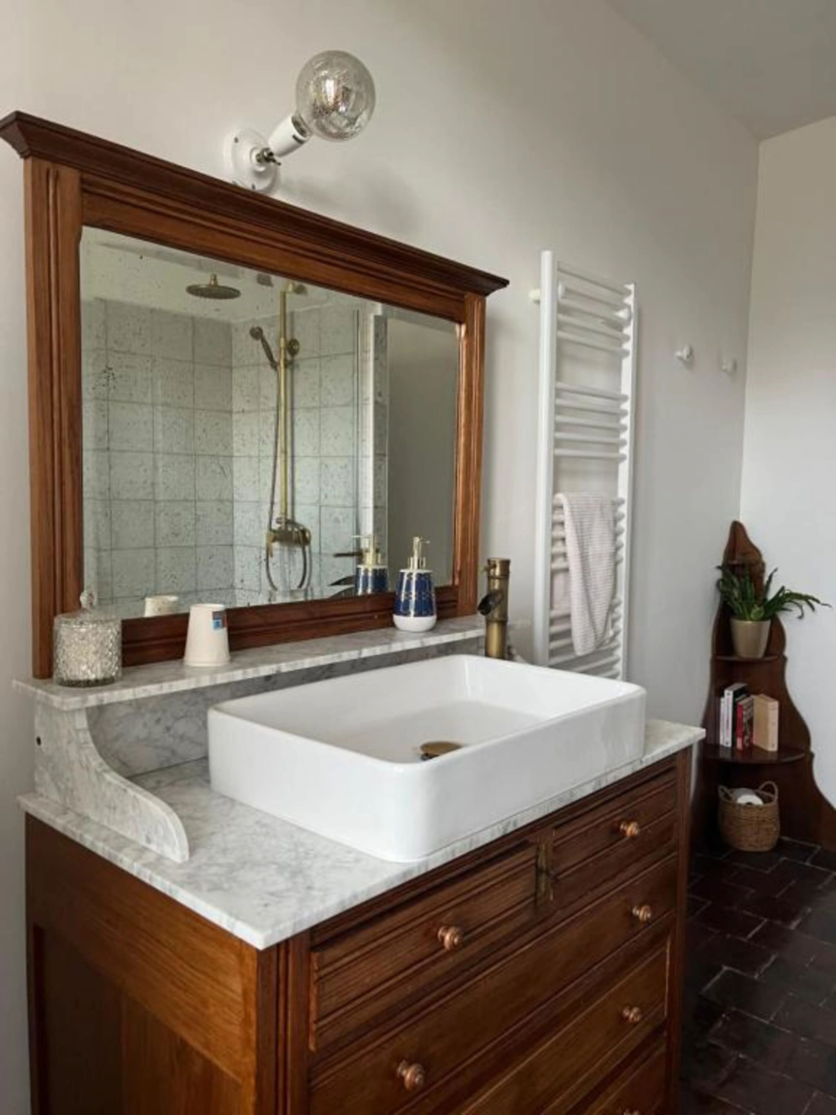A bathroom with a large mirror, a white sink, wooden cabinetry, a towel rack, and a shower.