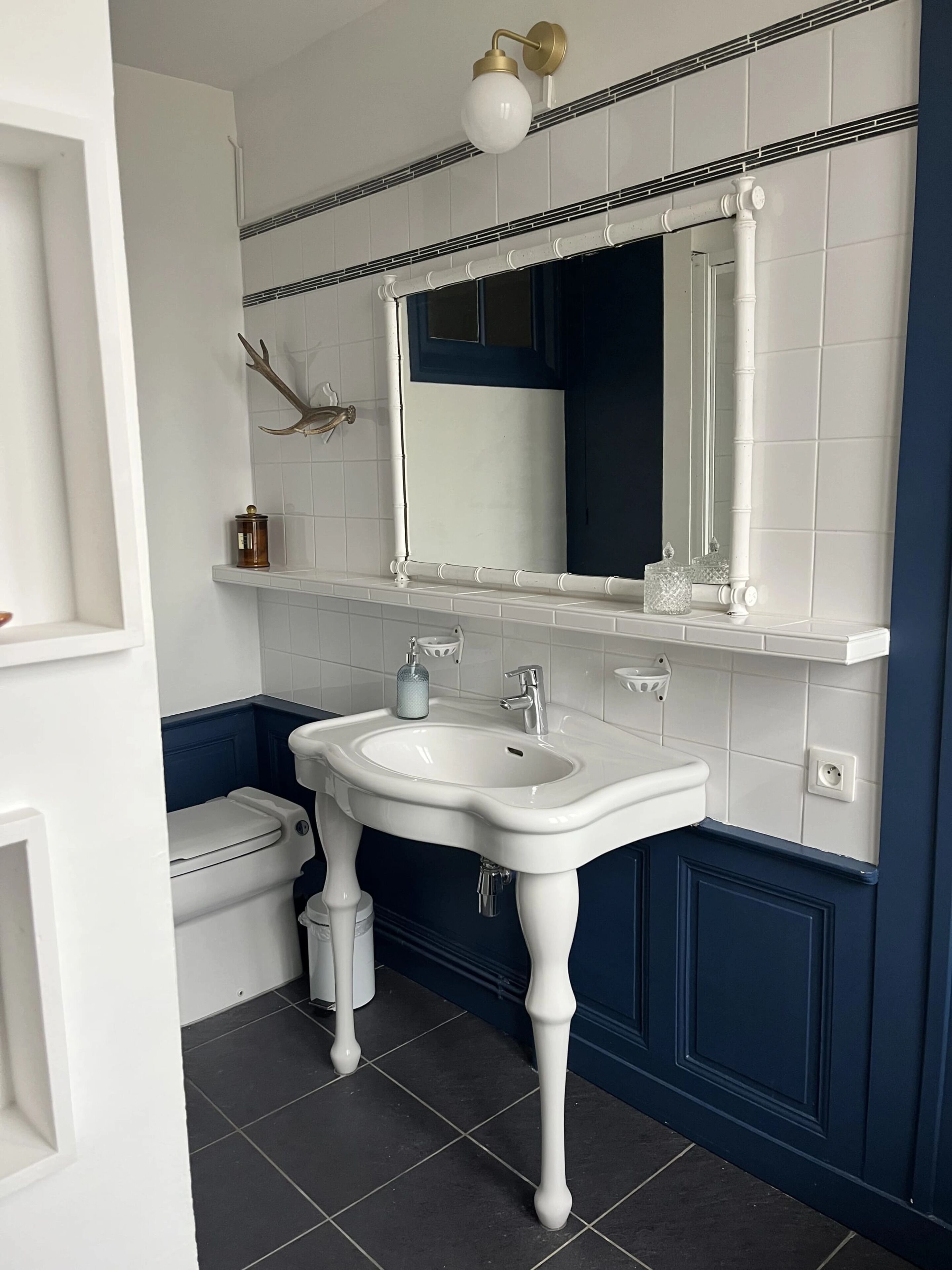 A bathroom with a white sink, dark blue walls, a white toilet, and a mirror above the sink.
