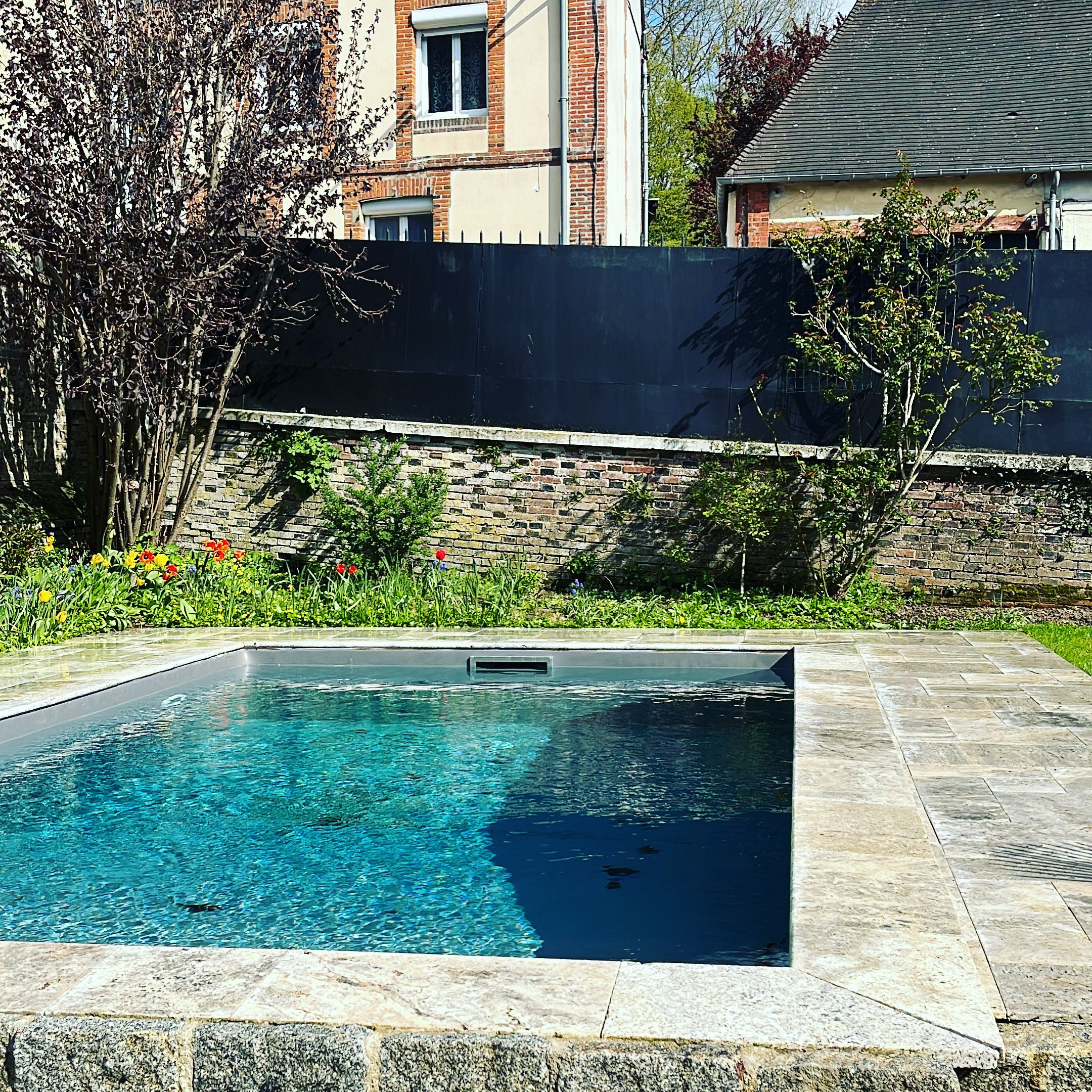 Een zwembad met helderblauw water, omgeven door een stenen terras en een bakstenen muur.