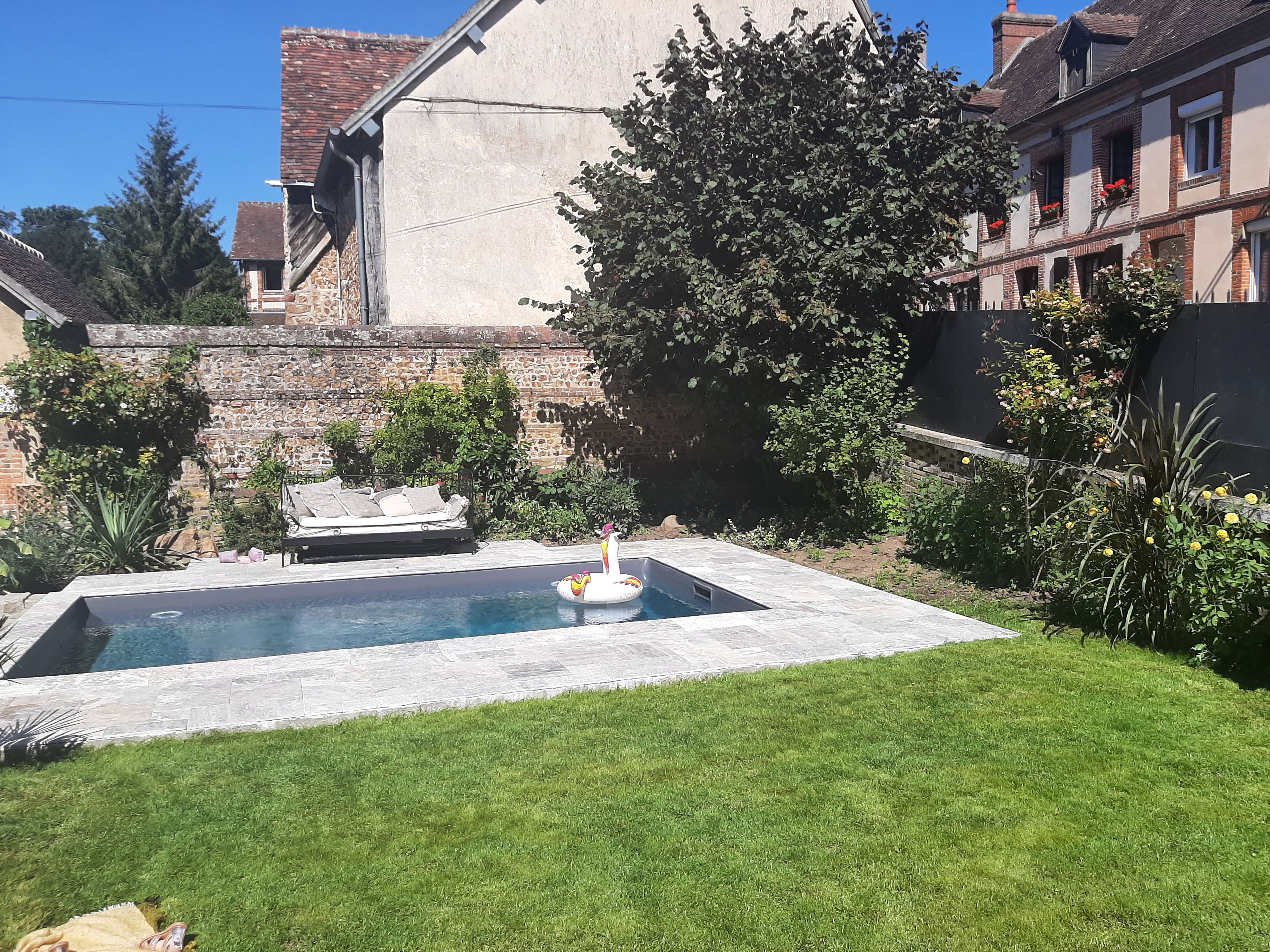 A swimming pool with a lounge chair and an inflatable float, surrounded by a well-maintained lawn and a stone wall.