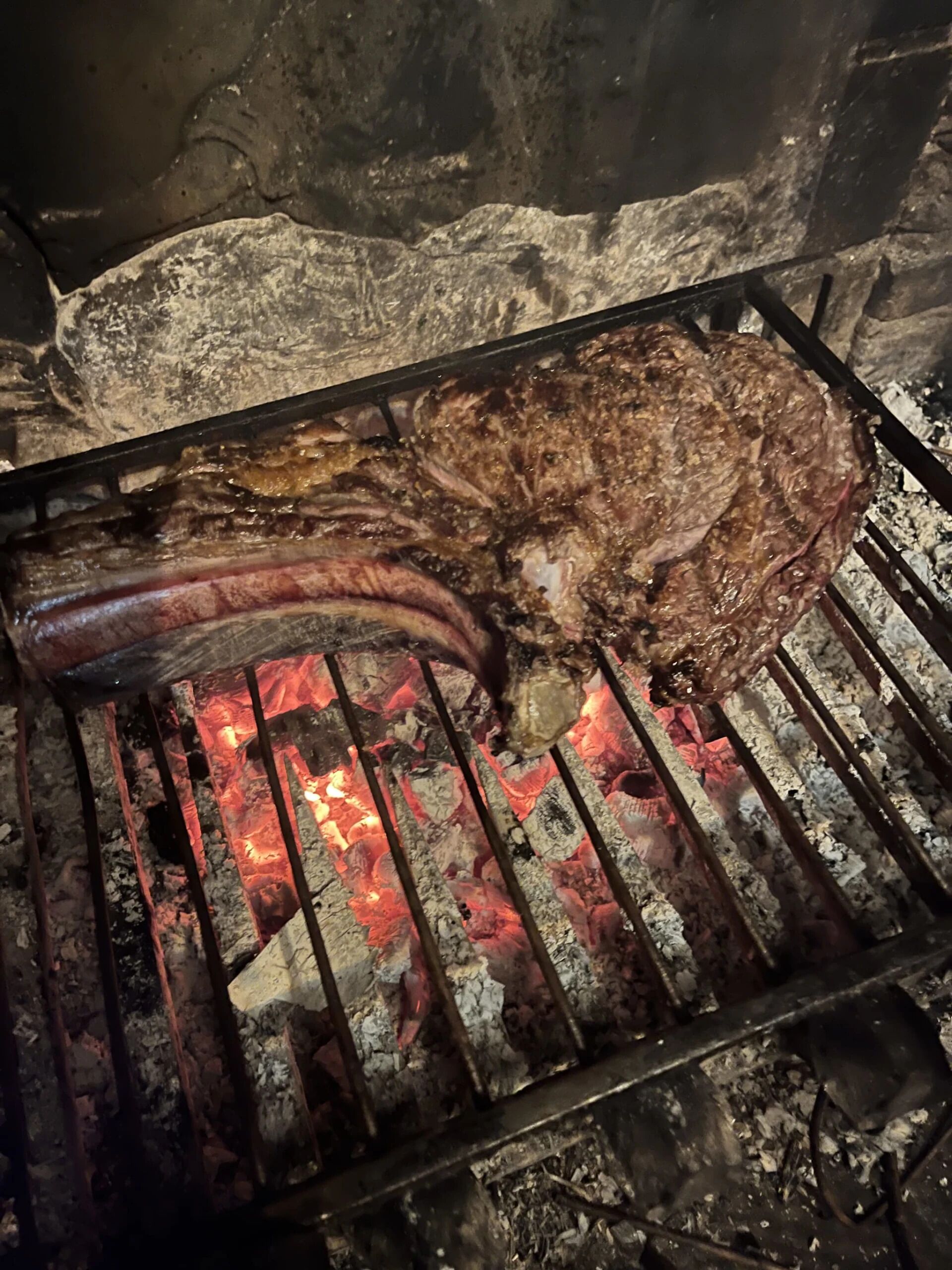 A grill with a large piece of meat and a sausage cooking over an open flame.