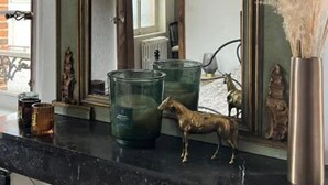 Ένα δωμάτιο με έναν μεγάλο καθρέφτη, ένα τζάκι και διακοσμητικά αντικείμενα τοποθετημένα πάνω στην επάνω επιφάνεια του τζακιού.
