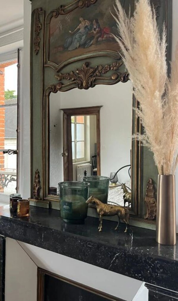 A room with a large mirror, a fireplace, and decorative items on the mantel. - L'ÉVIDENCE (Rugles)
