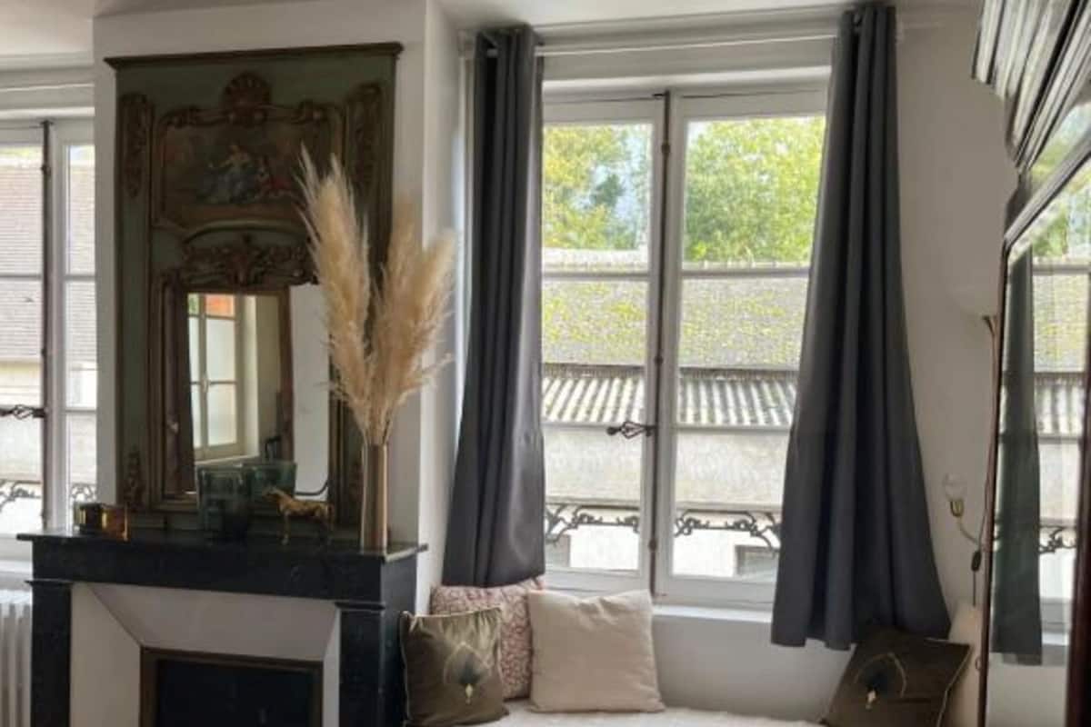 A room with a bed, a fireplace, a mirror, and large windows with curtains.