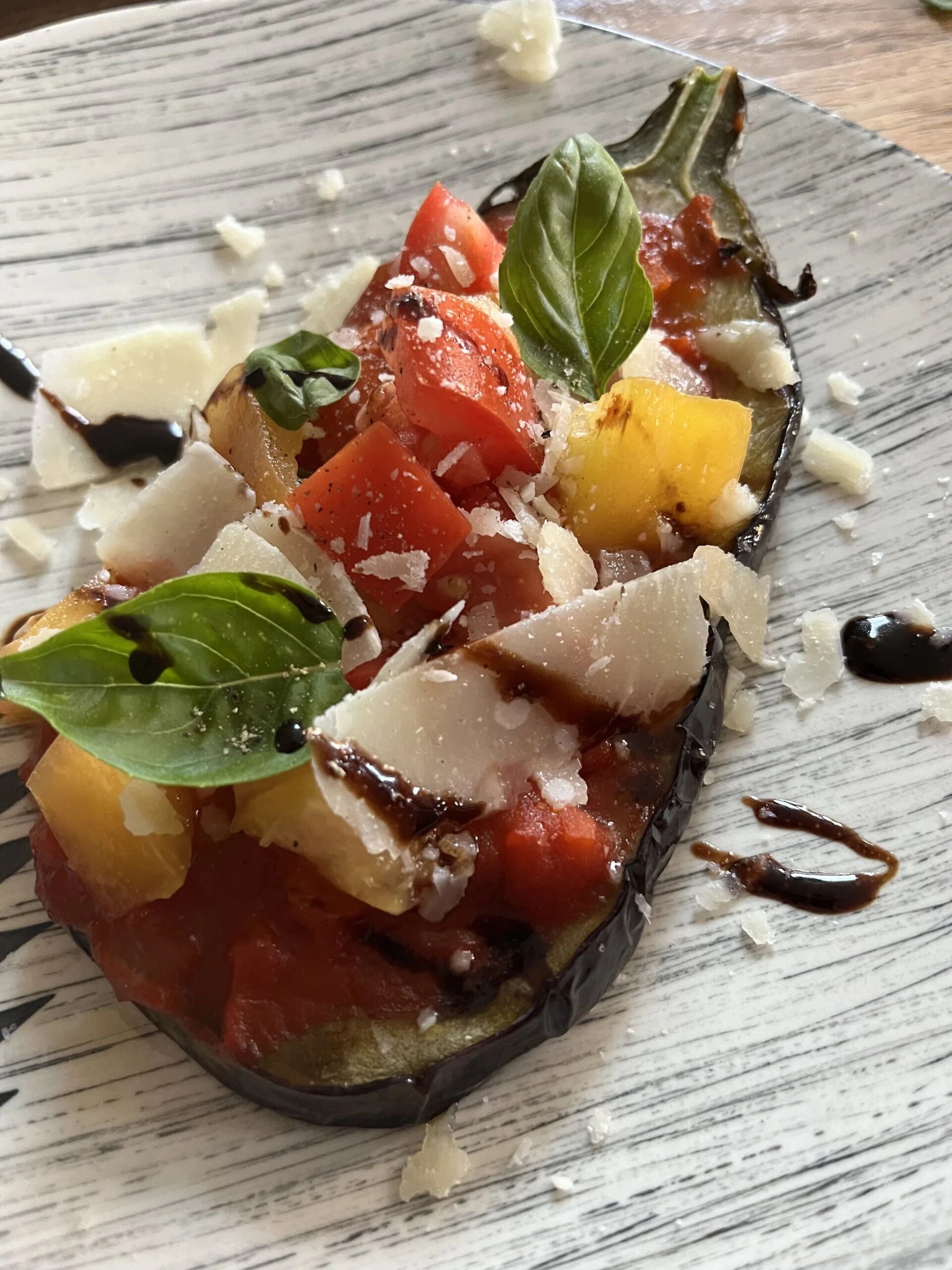 Un plato con berenjena asada, tomates y albahaca.