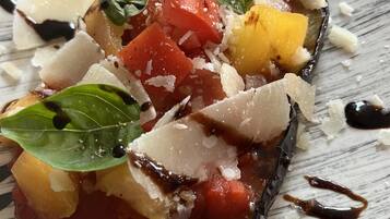 Un plato con berenjena asada, tomates y albahaca.