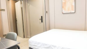 A hotel room with a bed, a desk, and a chair. There is a door and a wall-mounted artwork. - Unit 3.105/6 (Singapore)