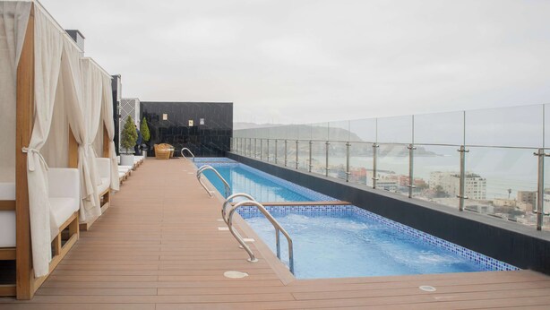 A rooftop swimming pool with a wooden deck, lounge chairs, and a glass balustrade. - w* | Distinctive 1BR w/ Balcony in Barranco (Barranco)