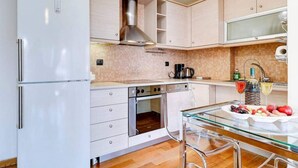 A modern kitchen with white cabinets, a stainless steel range hood, a built-in oven, and a glass dining table with chairs. - Brand new flat in the amazing area of       Alimos (Alimos)
