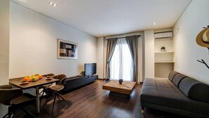 A modern living room with a dark sofa, a dining table with chairs, a flat-screen TV, and a coffee table. - Classy and stylish apartment next to Hilton (Athina)