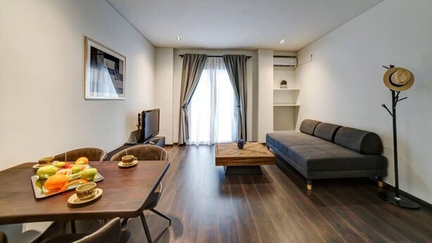 A modern living room with a sofa, a dining table with fruit, a TV, and a coat rack. - Classy and stylish apartment next to Hilton (Athina)