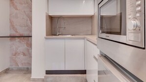 A modern kitchen with white cabinetry, a stainless steel sink, and a built-in microwave. - Nancy   s studio at metro Petralona (Athina)