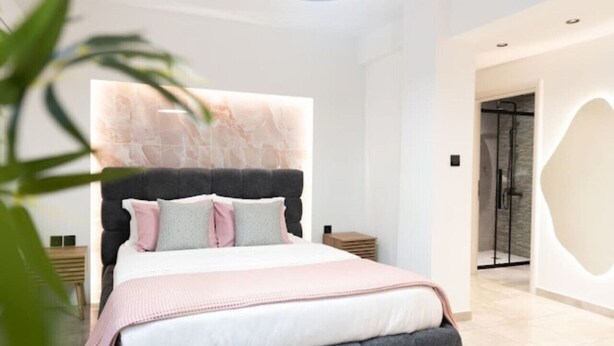 A modern bedroom with a large bed, a headboard with a light fixture, a bedside table, and a walk-in closet. - Nancy   s studio at metro Petralona (Athina)