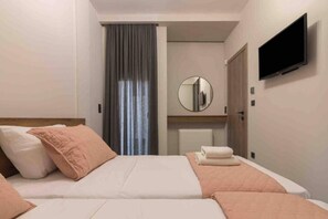 Ett hotellrum med en säng, en tv som är monterad på väggen, en spegel och ett fönster med gardiner.