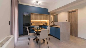 A modern kitchen with blue cabinetry, a dining area with a table and chairs, and a wooden door. - Blue Pearl at Glufada sea side (Glifada)