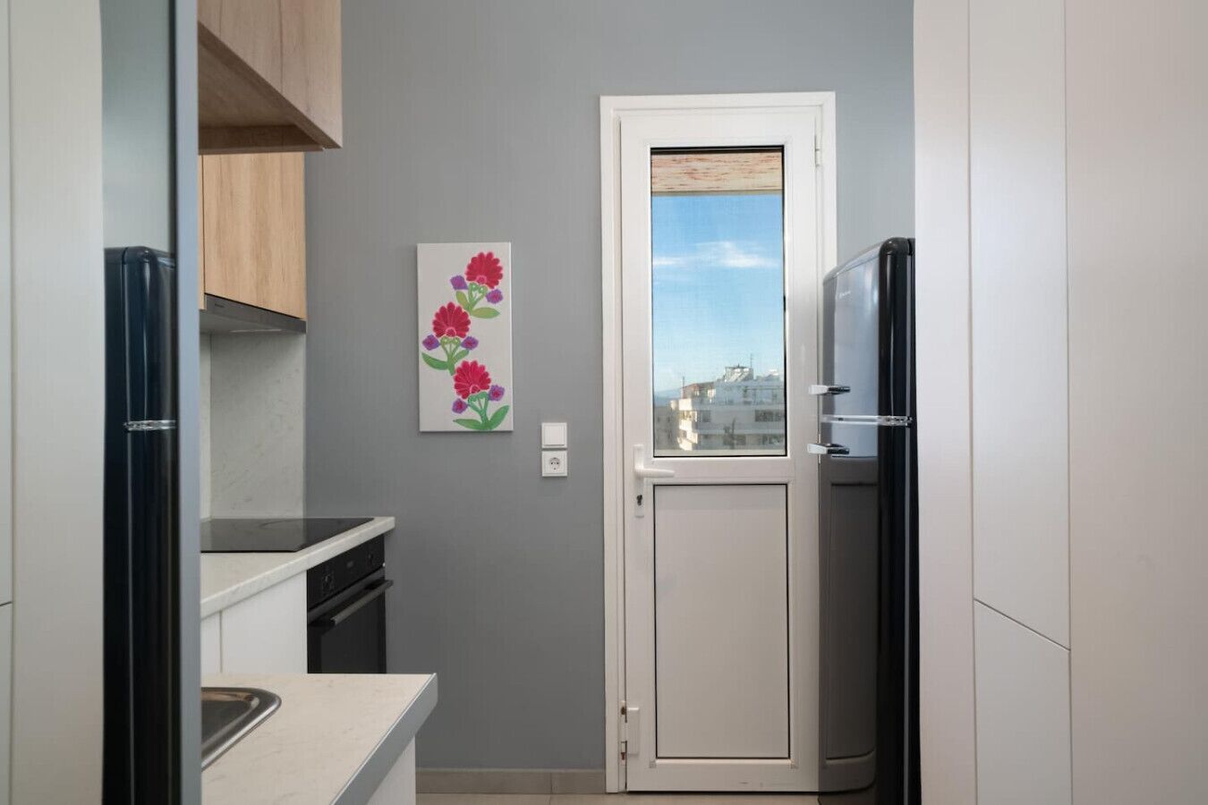 Une cuisine compacte équipée d’un réfrigérateur, d’un évier et d’une fenêtre donnant sur des immeubles.