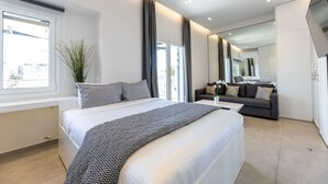 A modern bedroom with a large bed, a sofa, a TV, and a window with curtains. - Jacuzzi Lux penthouse P Faliro (Paleo Faliro)