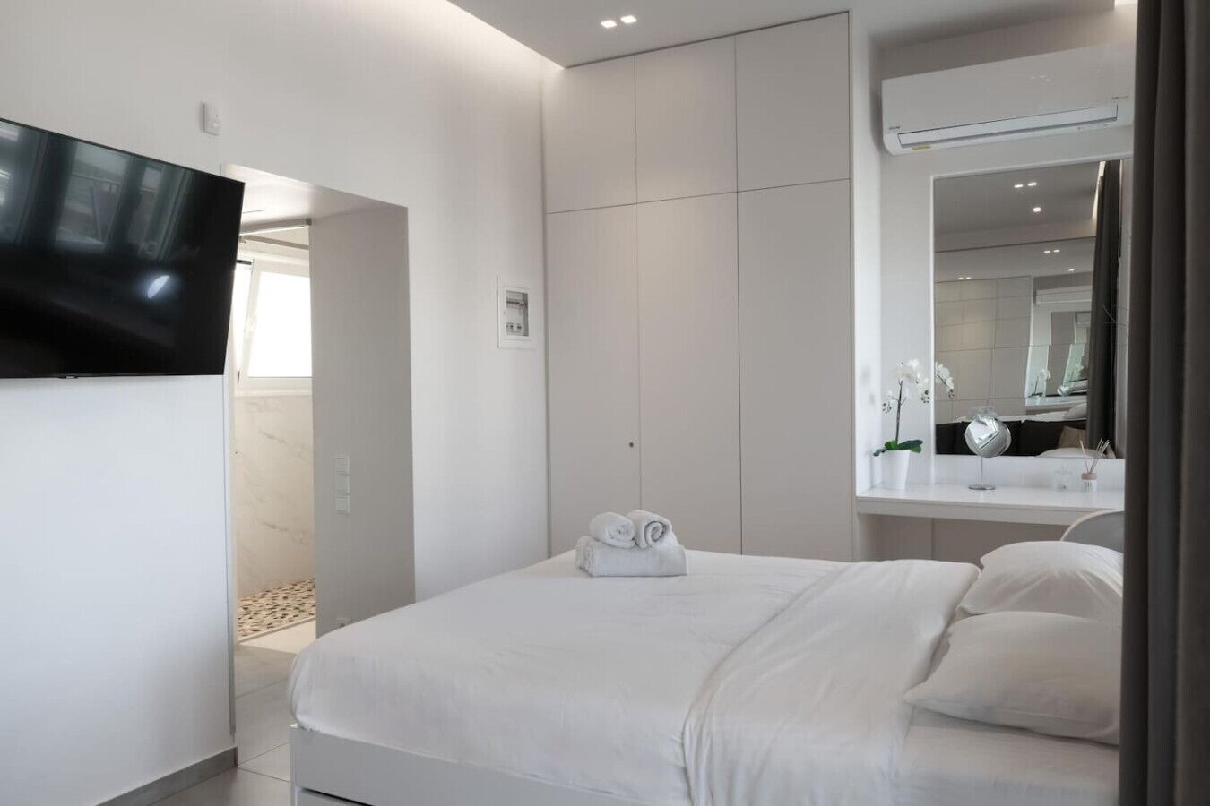 Ett modernt hotellrum med en stor säng, en platt-TV som är monterad på väggen, en stor spegel och en liten krukväxt.