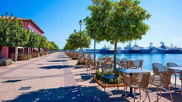 Eine Uferpromenade mit Außenplätzen und Booten im Hintergrund.