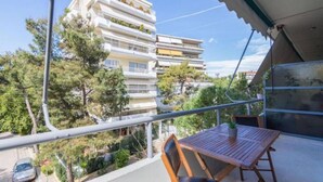 Uma varanda com mesa e cadeiras de madeira, com vista para uma área residencial com edifícios altos e árvores.