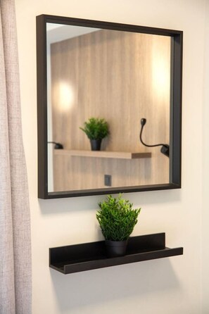 A mirror with a black frame mounted on a wall, above a black shelf holding a potted plant.