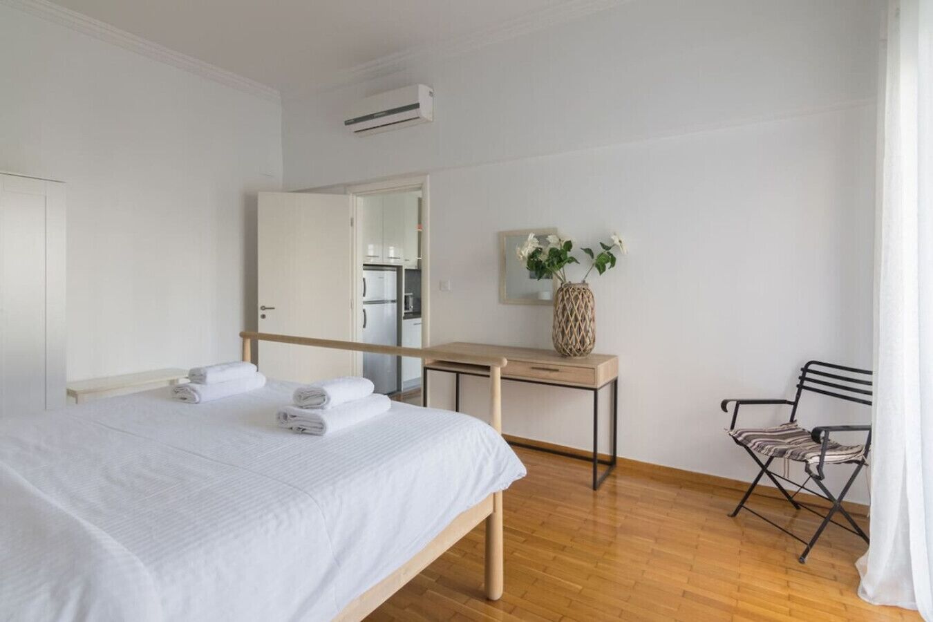 A hotel room with a bed, a desk, a chair, a mirror, and a door leading to the kitchen.